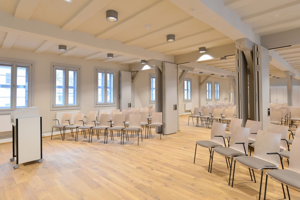 Fenster auf beiden Längsseiten des Raumes schaffen einen hellen Veranstaltungssaal, der mit moderner Technik ausgestattet ist