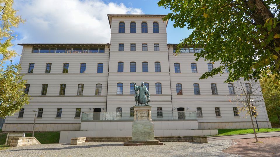 Ansicht der weißen Fasssade aus Stein des Gebäudes am östlichen Ende des Lindenhofs mit dem Francke-Denkmal davor. 