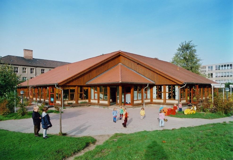 Ein moderner Holzbau mit bodentiegen Fenstern inmitten einer Wiese lädt kinder in die Kita August Hermann Francke ein. 